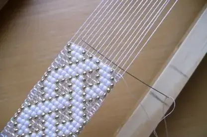 Výroba náramku z korálků na malém , dřevěném strojku.